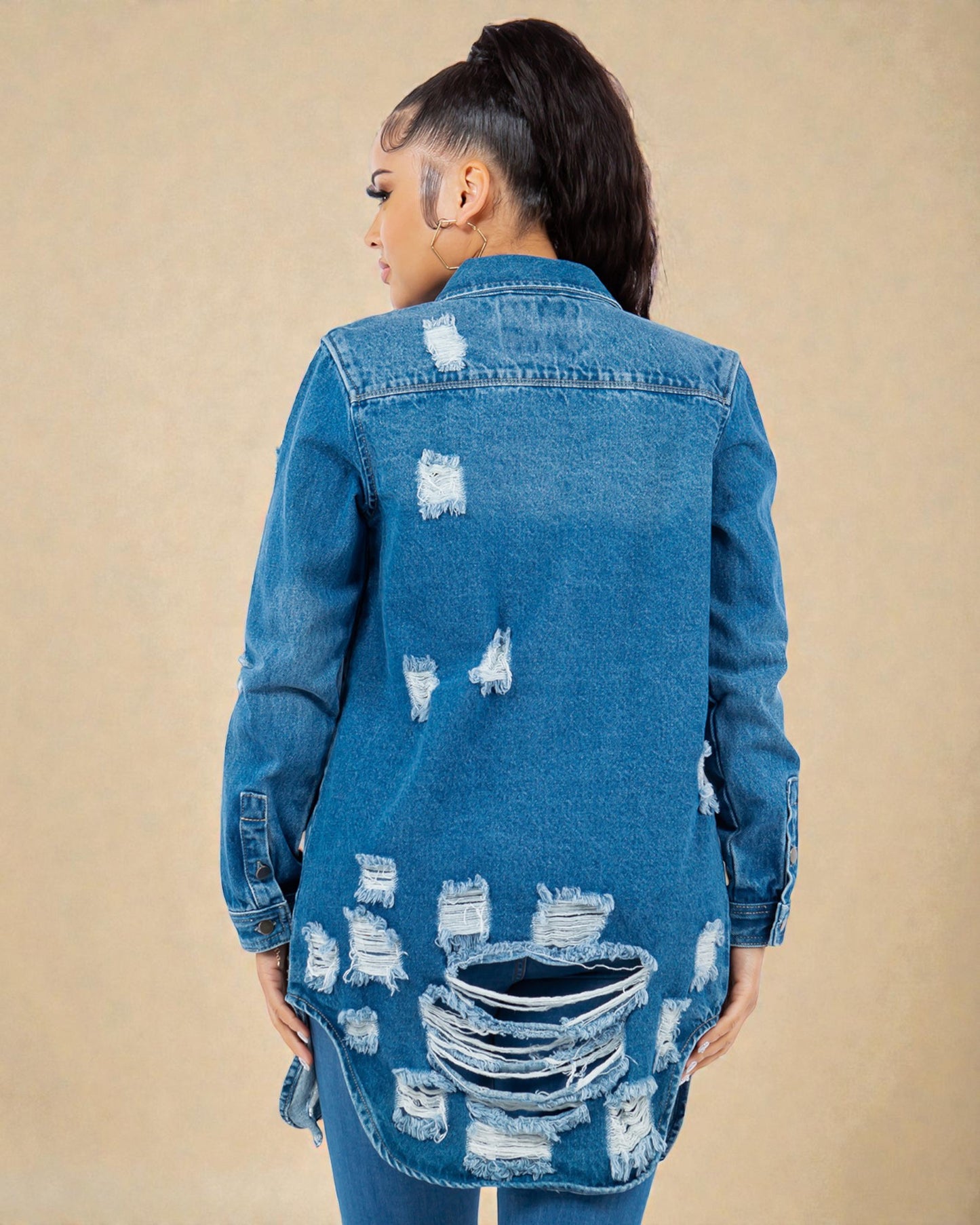 Person wearing a distressed blue denim jacket on a beige background