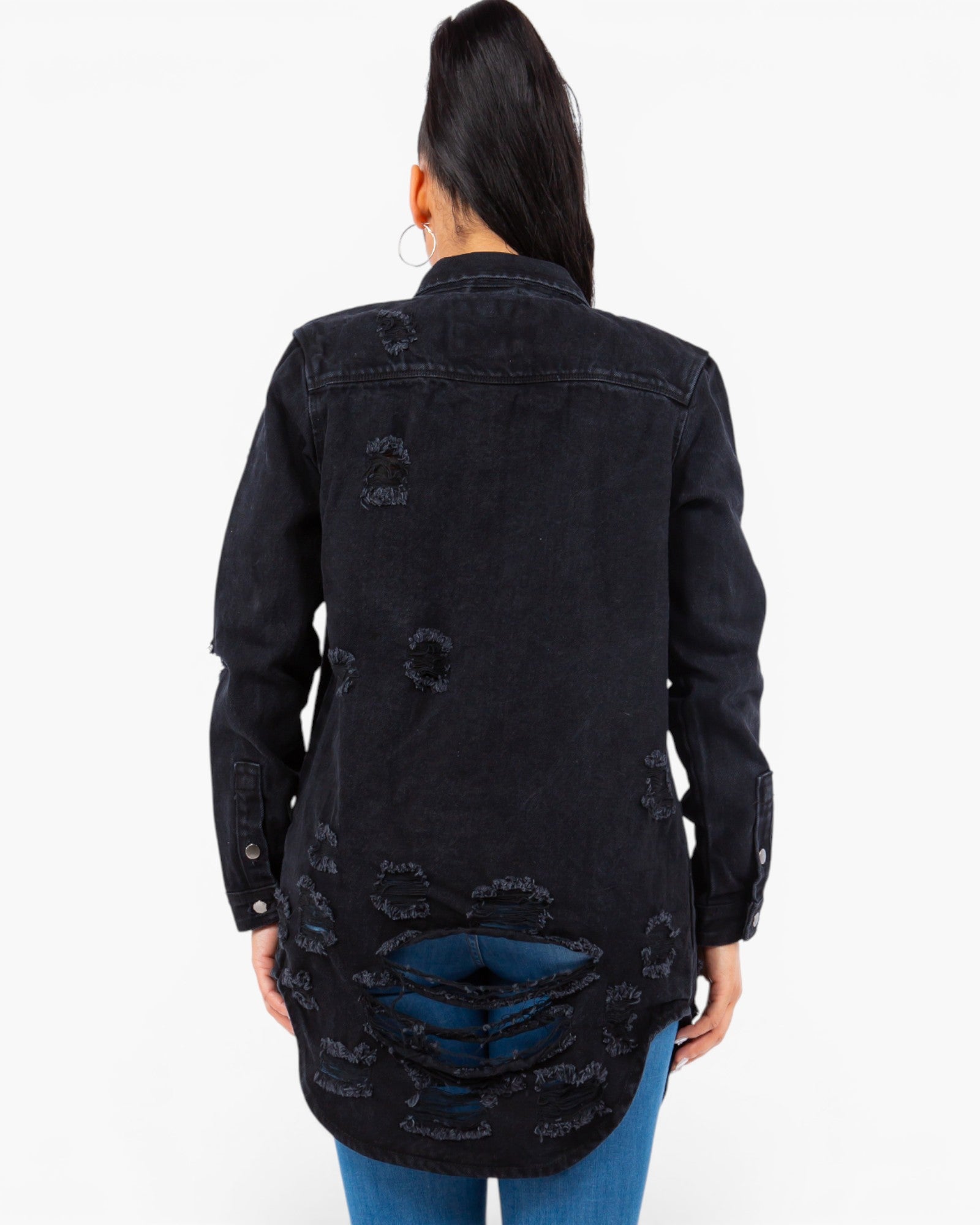 A woman viewed from the back wearing a black distressed denim jacket with ripped details and blue jeans, against a plain white background.