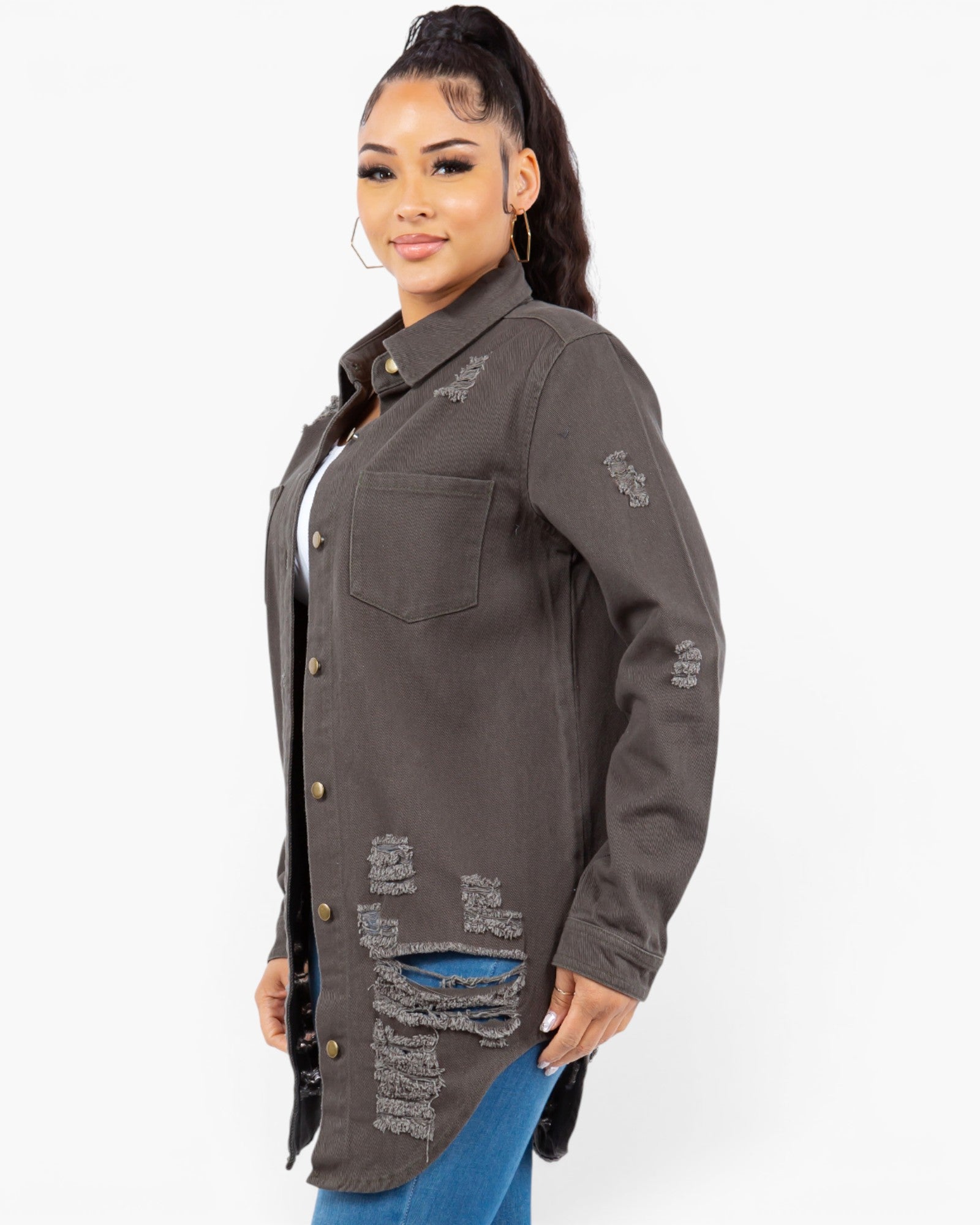 A woman wearing a dark gray distressed button-up shirt jacket with ripped details, paired with blue jeans and a white top, photographed against a light gray studio background.