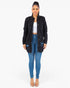 A woman modeling a black distressed denim jacket over a white crop top and blue skinny jeans, standing against a plain white studio background.