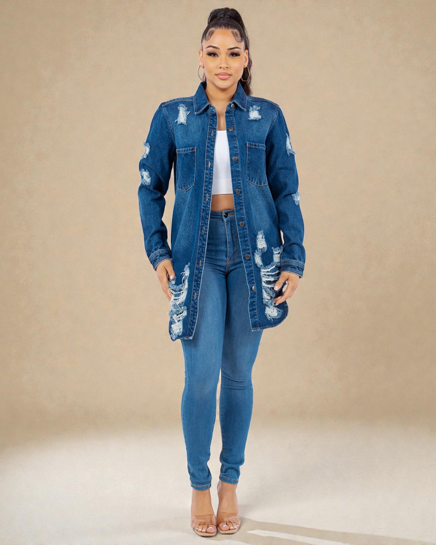 Woman wearing a distressed denim jacket and jeans on a beige background