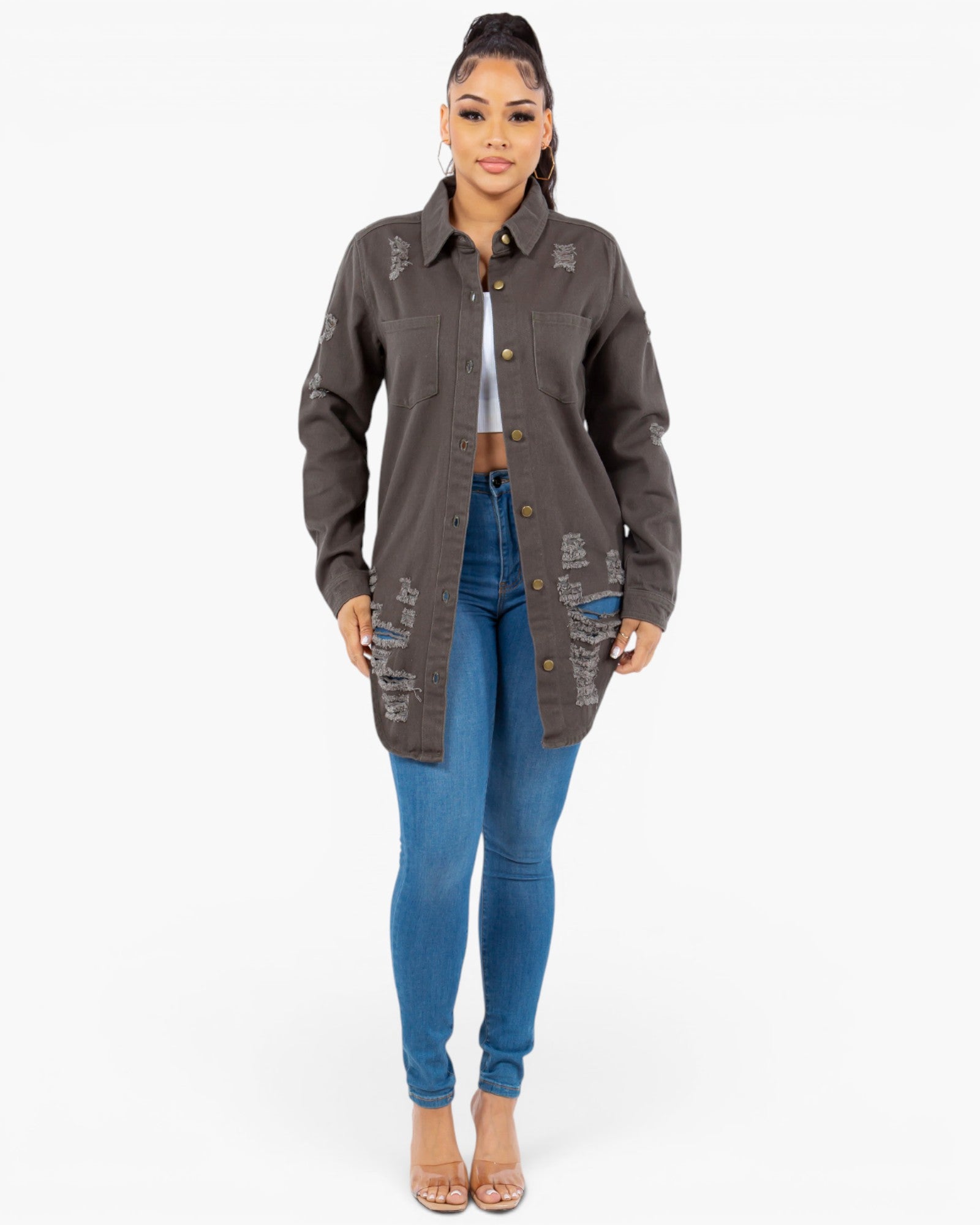 A woman modeling a dark brown distressed utility jacket with button details, worn over a white crop top and blue skinny jeans, against a plain white background.