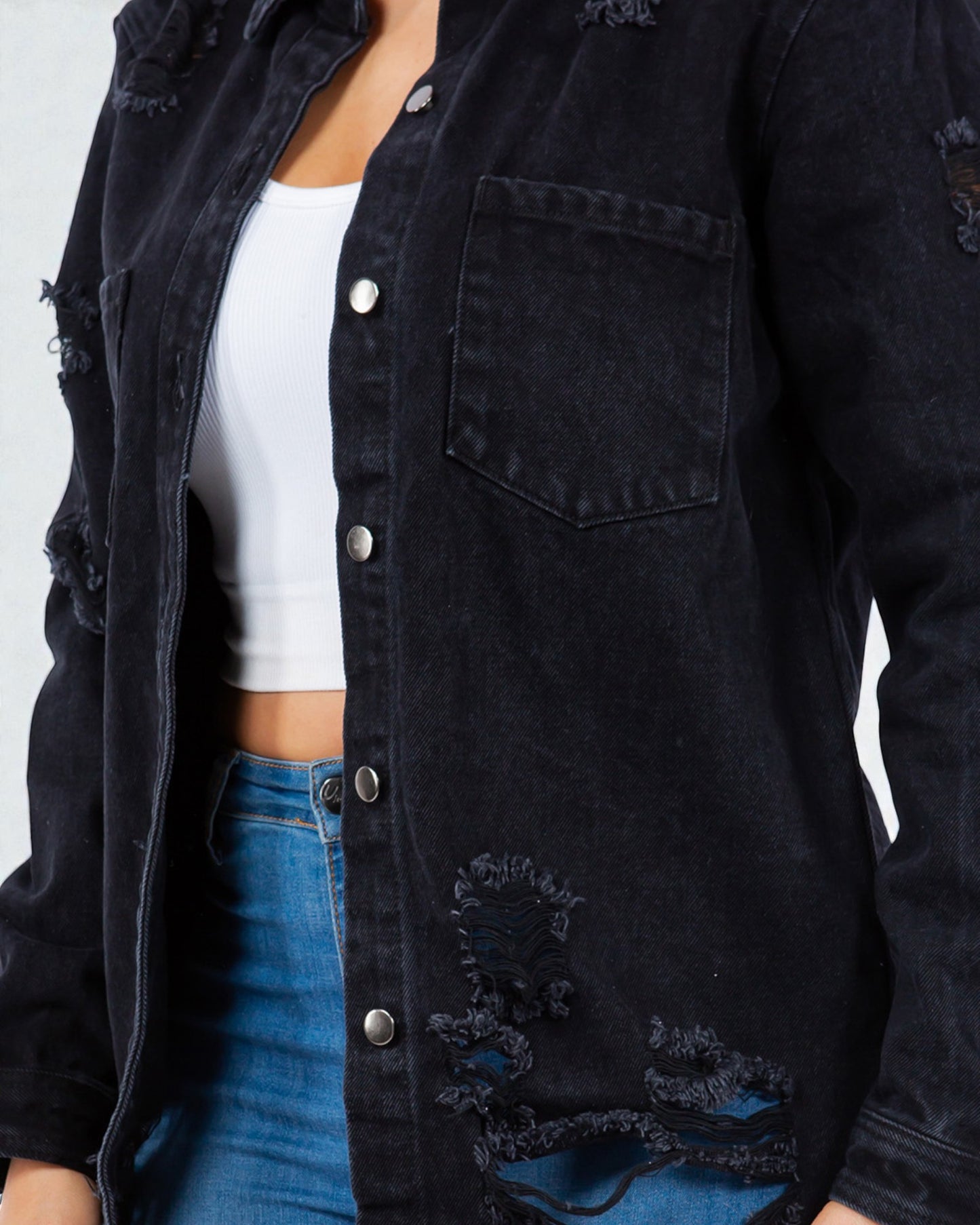 Person wearing a black distressed denim jacket over a white top and blue jeans on a white background