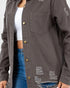 A close-up of a person wearing a dark gray distressed button-up shirt jacket over a white crop top and blue jeans, showing the chest pocket, brass-tone buttons, and frayed details.