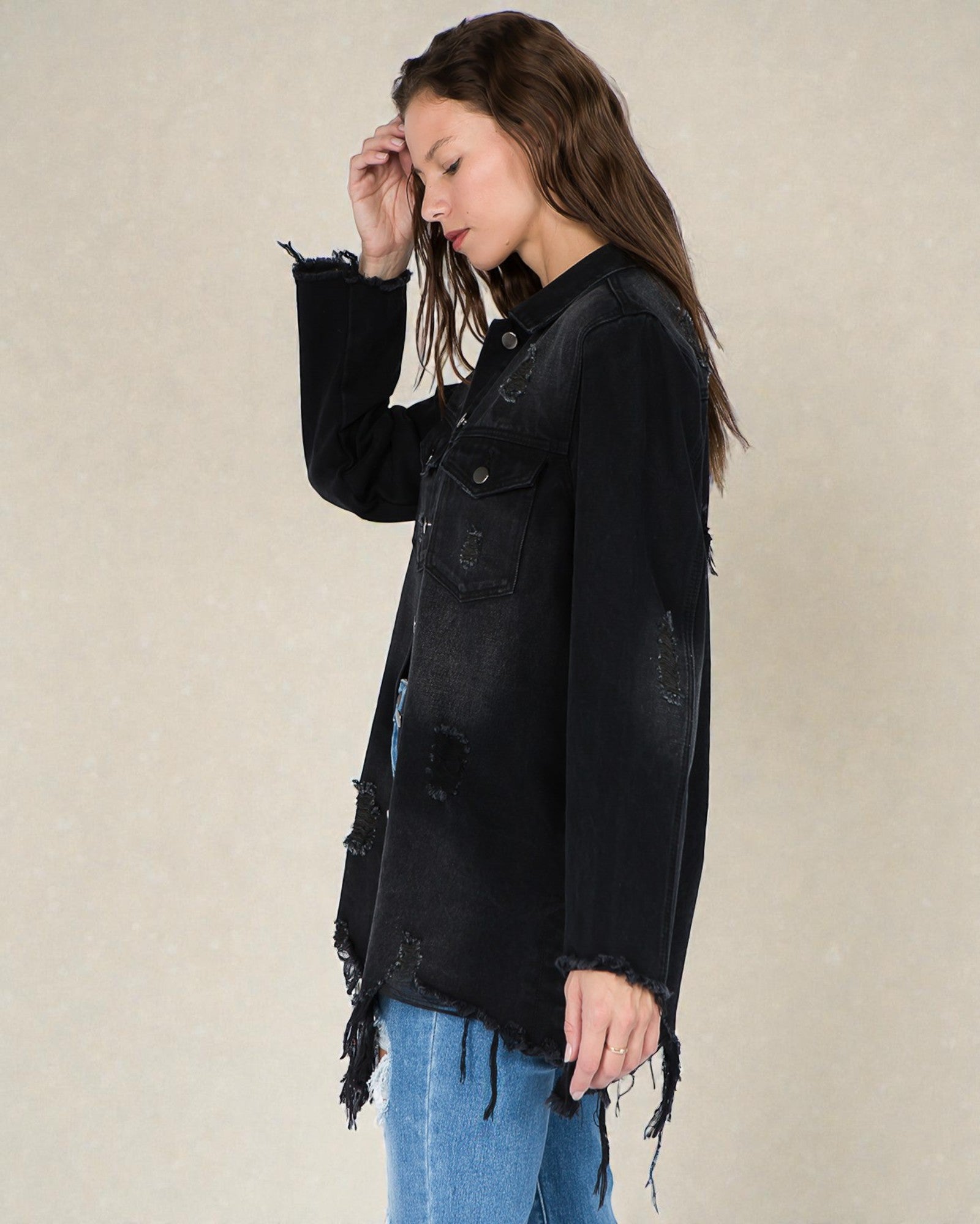 Woman wearing a black distressed denim jacket against a beige background