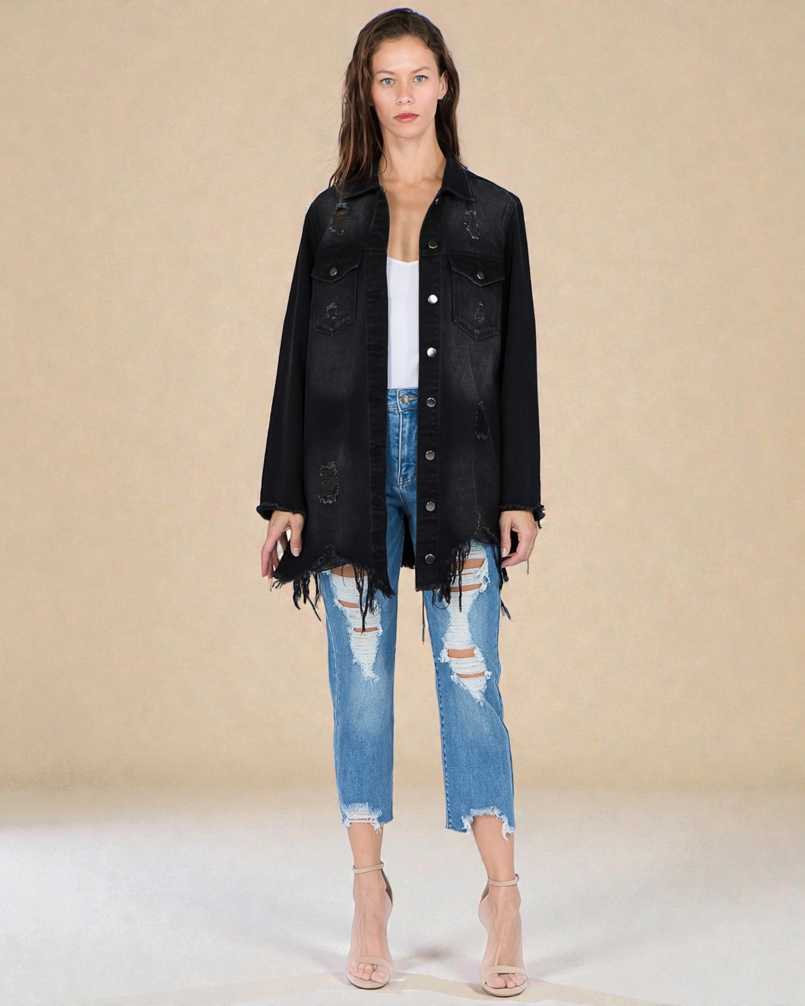 Woman wearing a black denim jacket and ripped jeans on a beige background