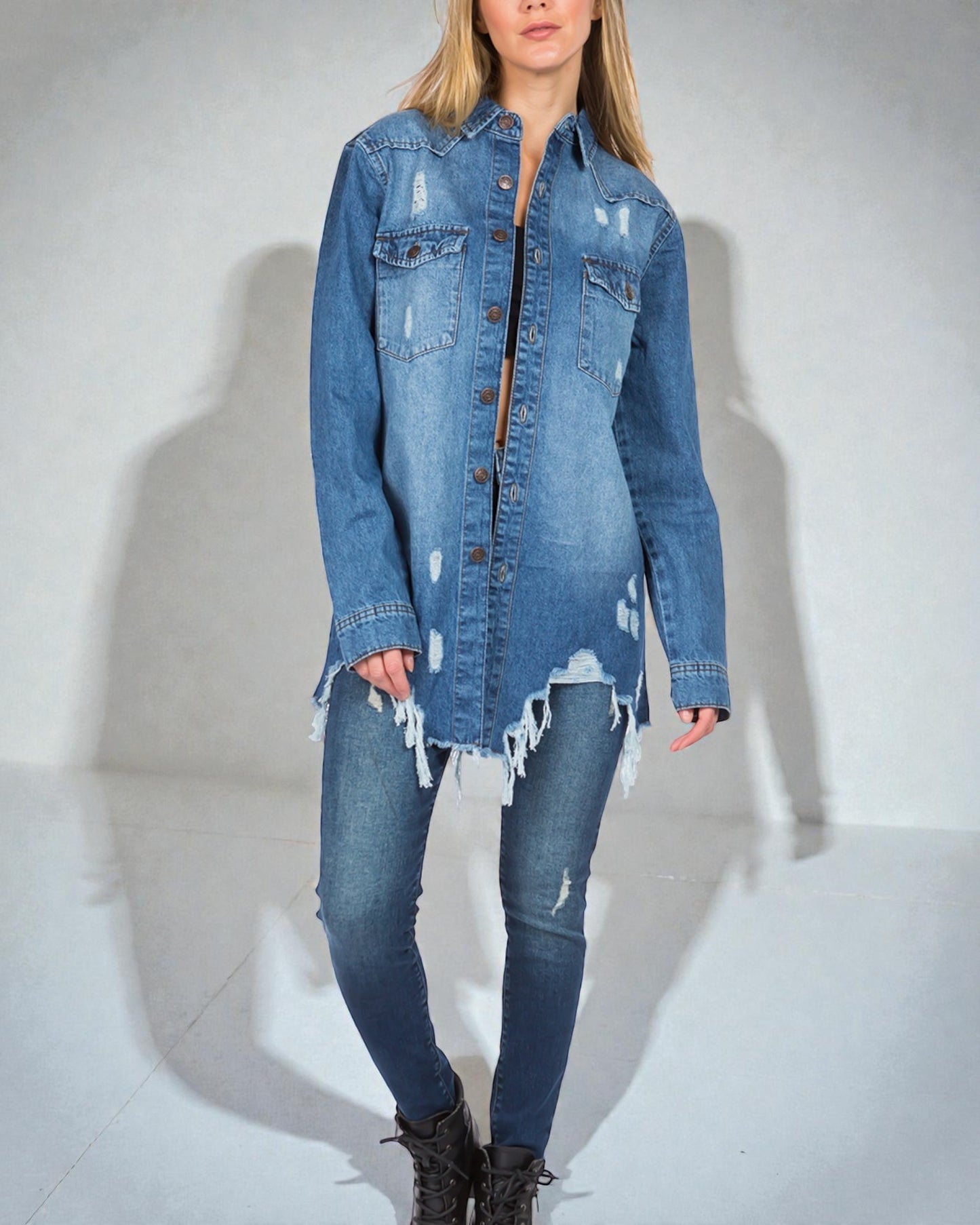 Person wearing a distressed denim jacket and jeans on a plain background