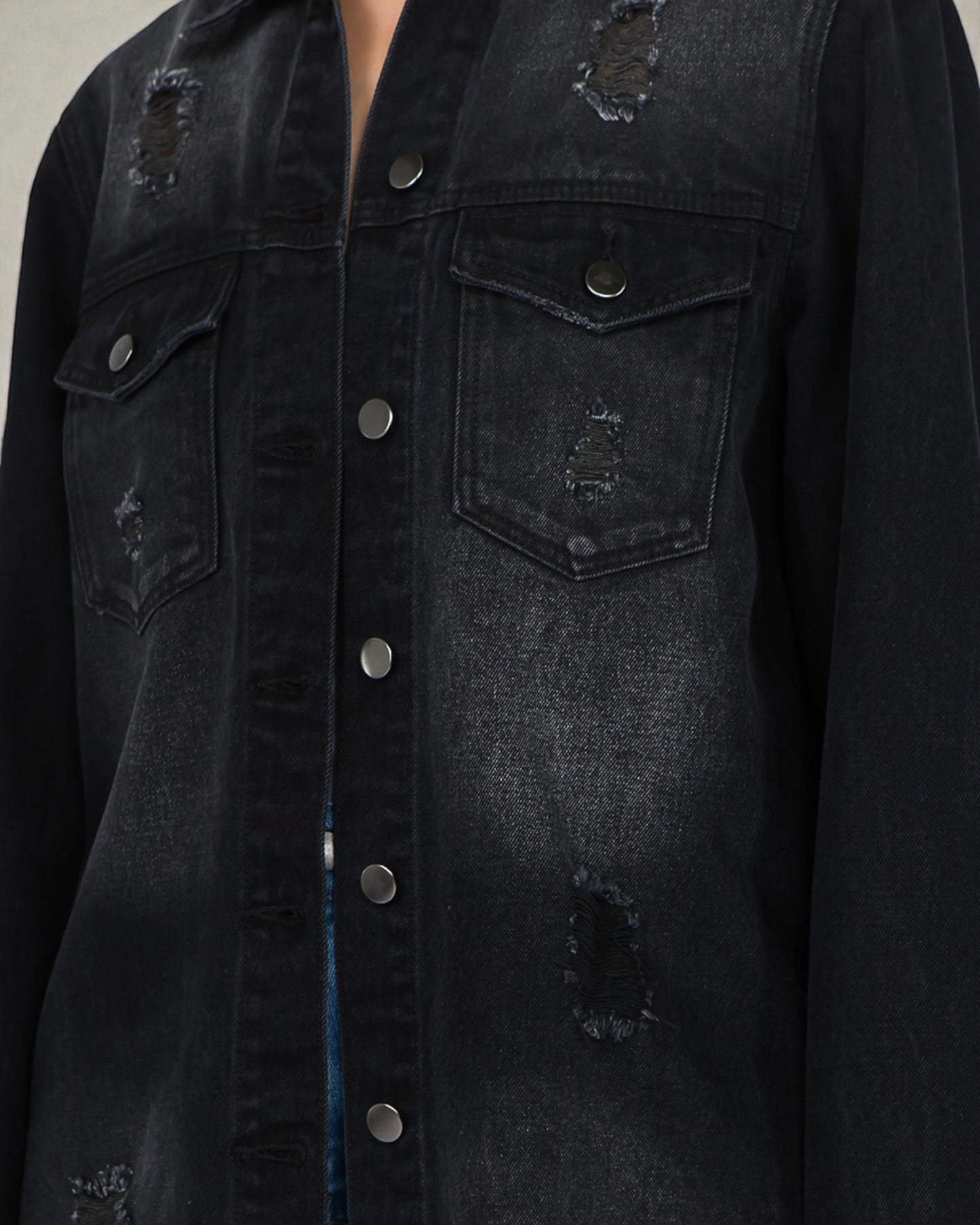 Black denim jacket with distressed details on a neutral background