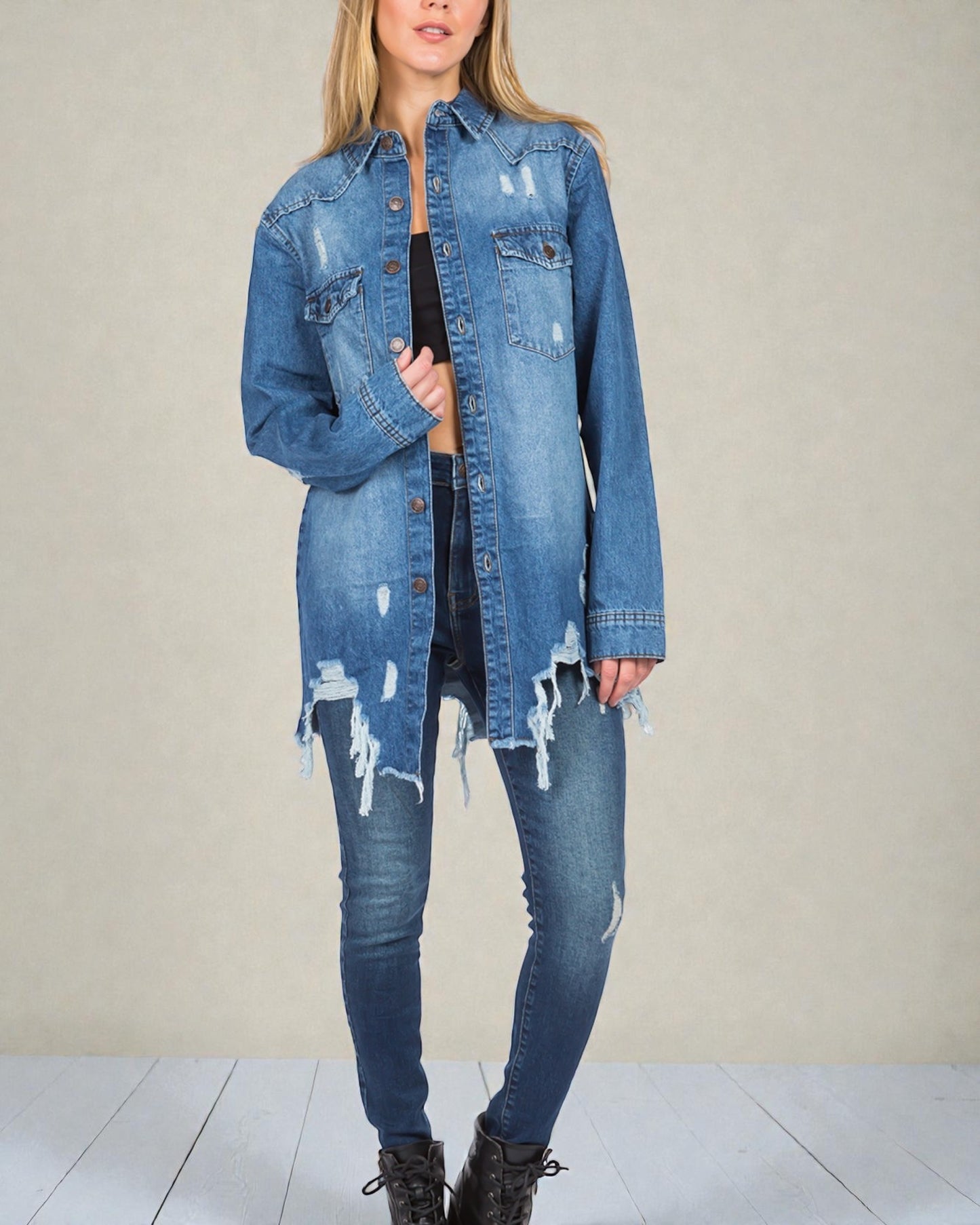 Person wearing a distressed denim jacket and jeans on a plain background