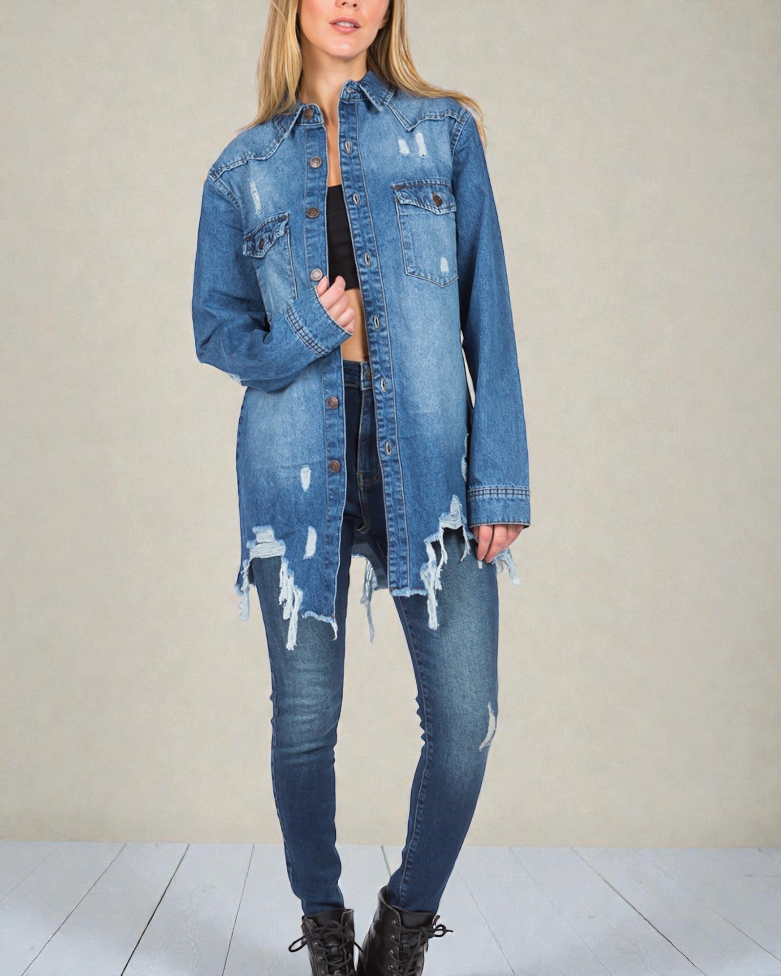 Person wearing a distressed denim jacket and jeans on a plain background