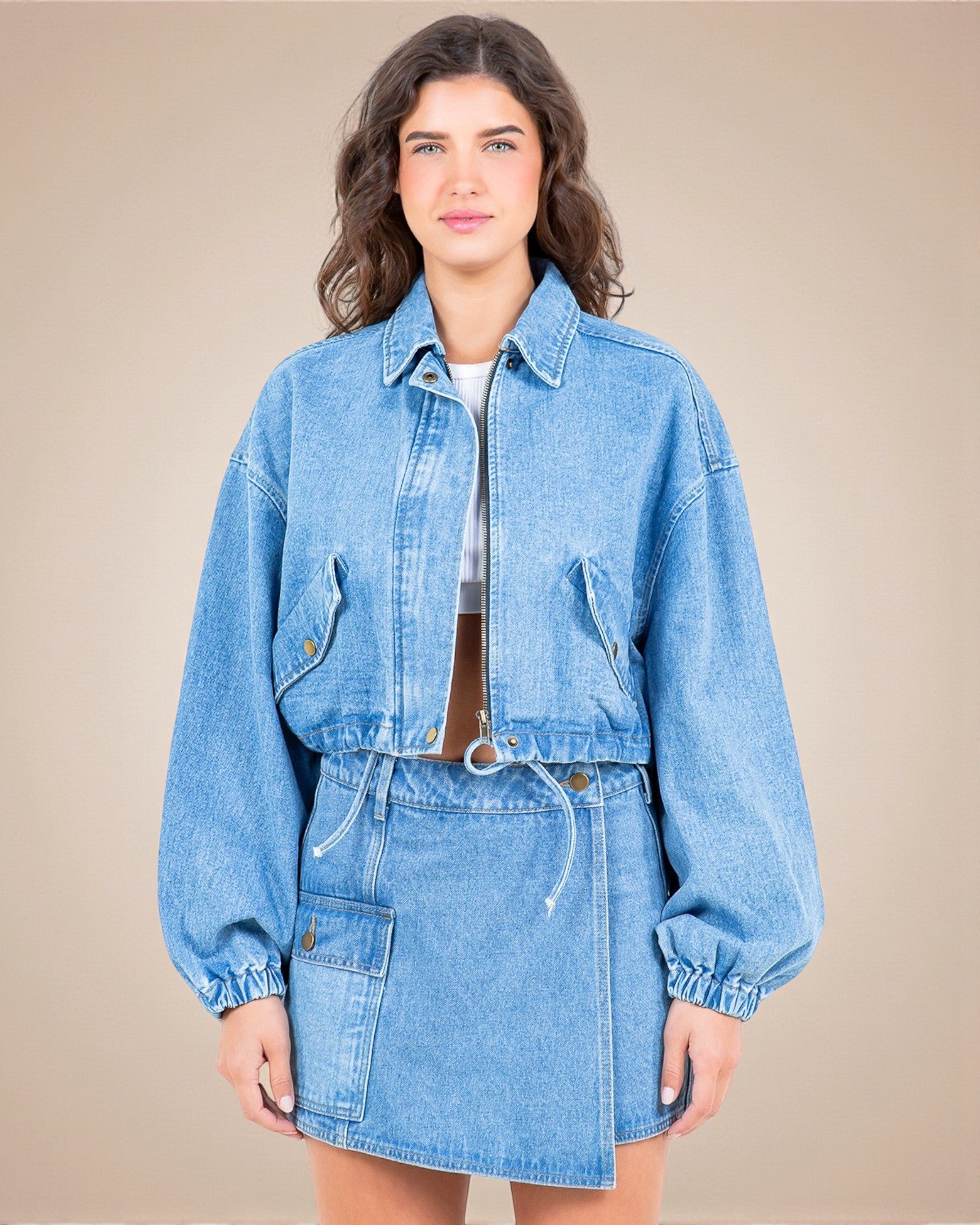 Woman wearing a blue denim jacket and skirt set against a beige background
