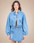 Woman wearing a blue denim jacket and skirt set against a beige background