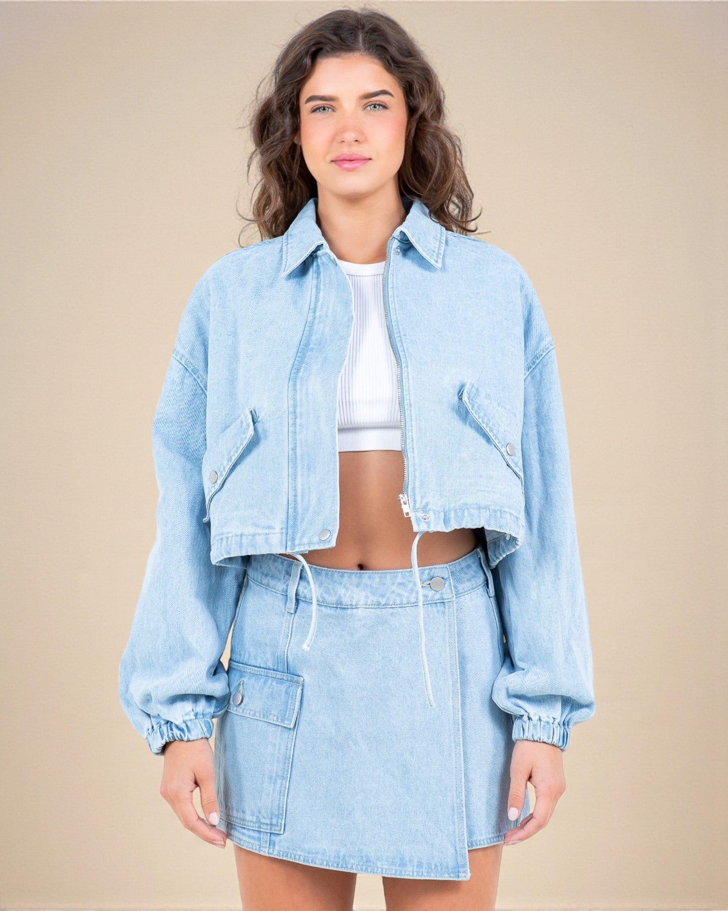 Woman wearing a light blue denim jacket and skirt set on a beige background
