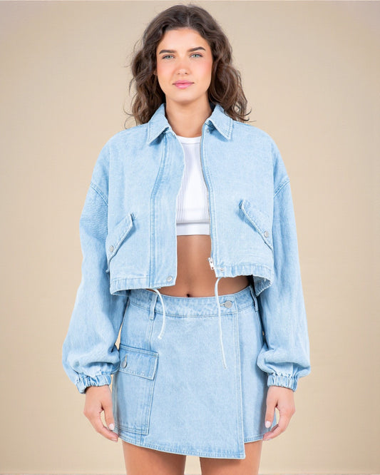 Woman wearing a light blue denim jacket and skirt set on a beige background