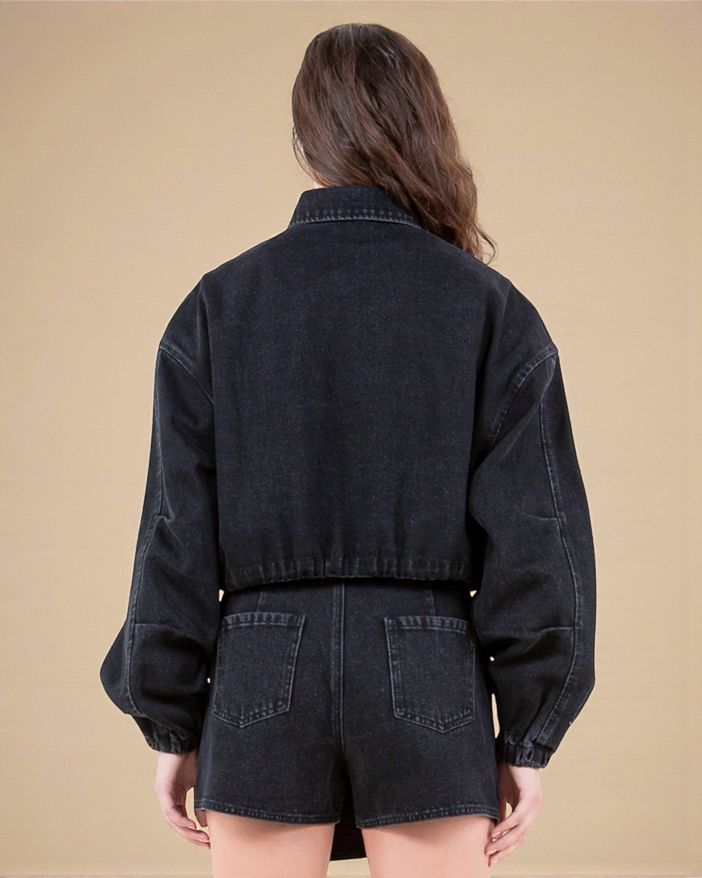 Person wearing a black denim jacket and shorts on a beige background