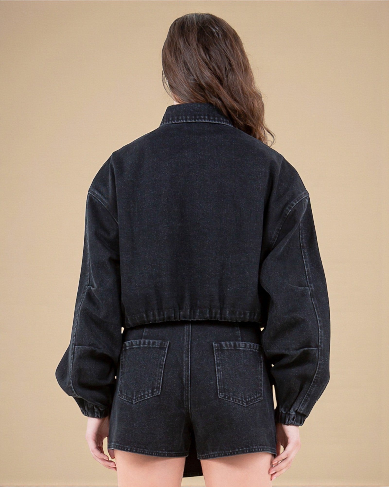 Person wearing a black denim jacket and shorts on a beige background