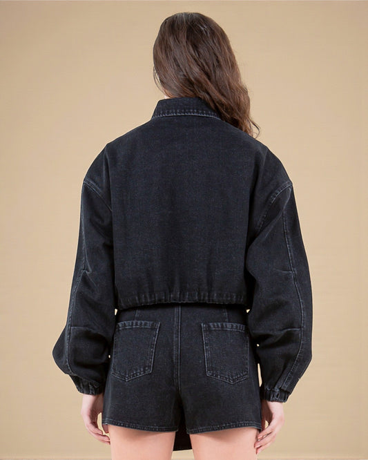 Person wearing a black denim jacket and shorts on a beige background