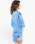 A woman shown in side profile wearing a light blue denim jacket and matching denim shorts against a plain white studio background.
