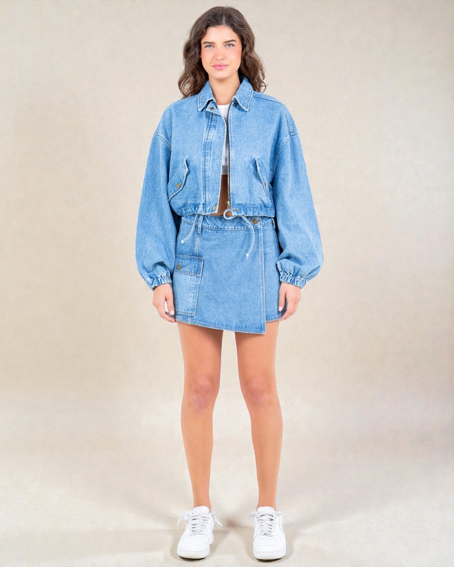 Person wearing a denim outfit with a jacket and skirt on a beige background
