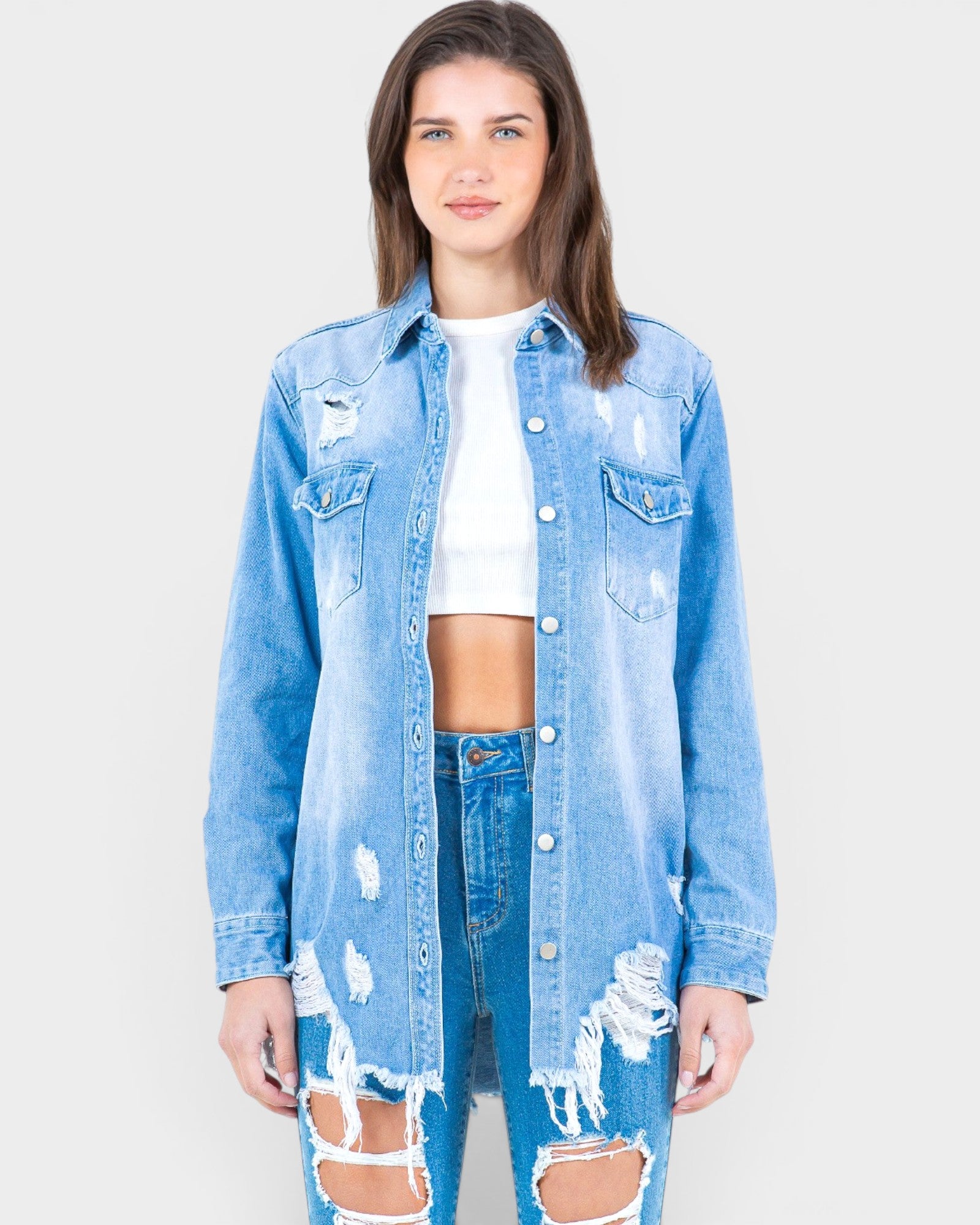 Woman wearing a distressed denim jacket and jeans on a plain background