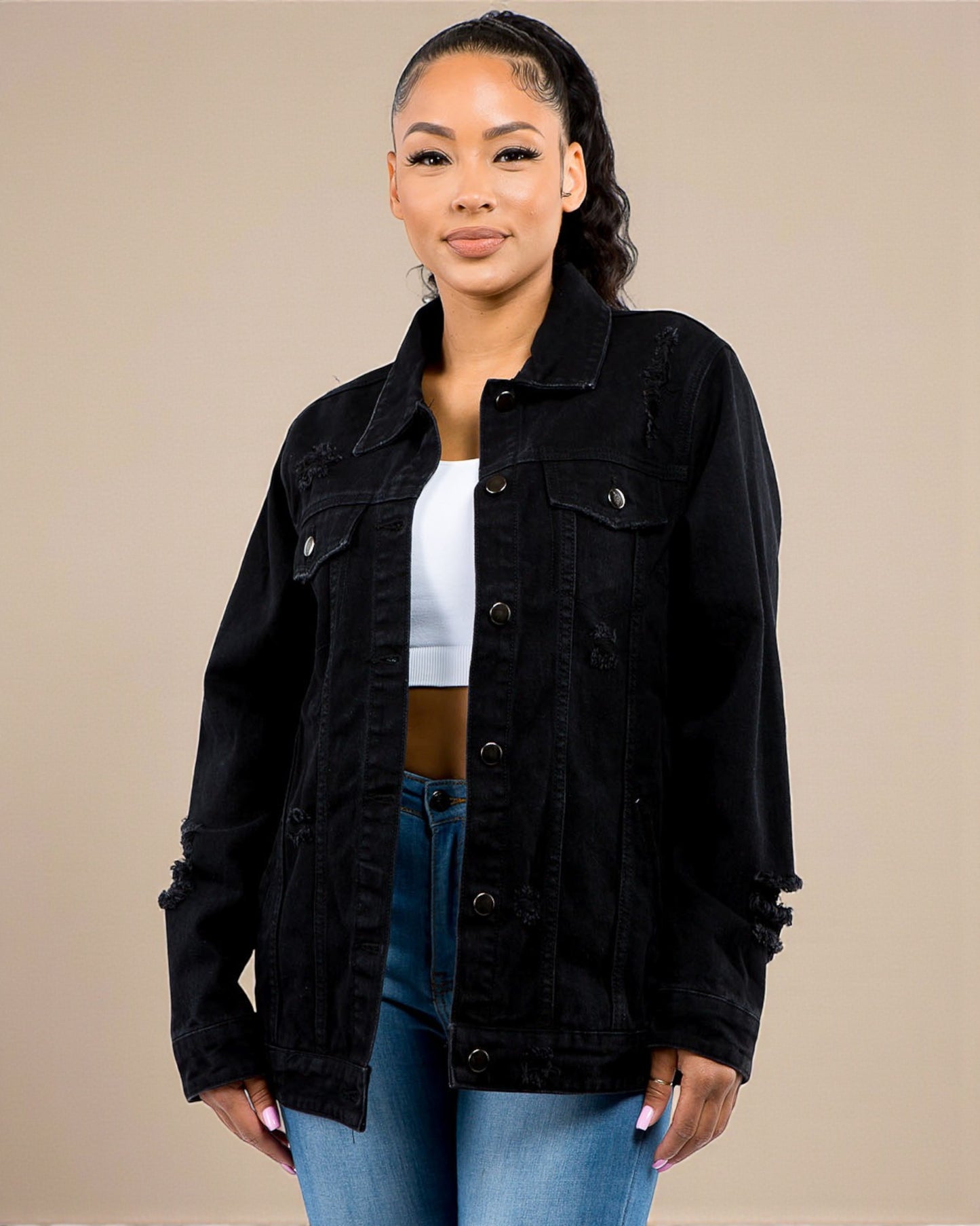 Woman wearing a black denim jacket over a white top and blue jeans on a beige background