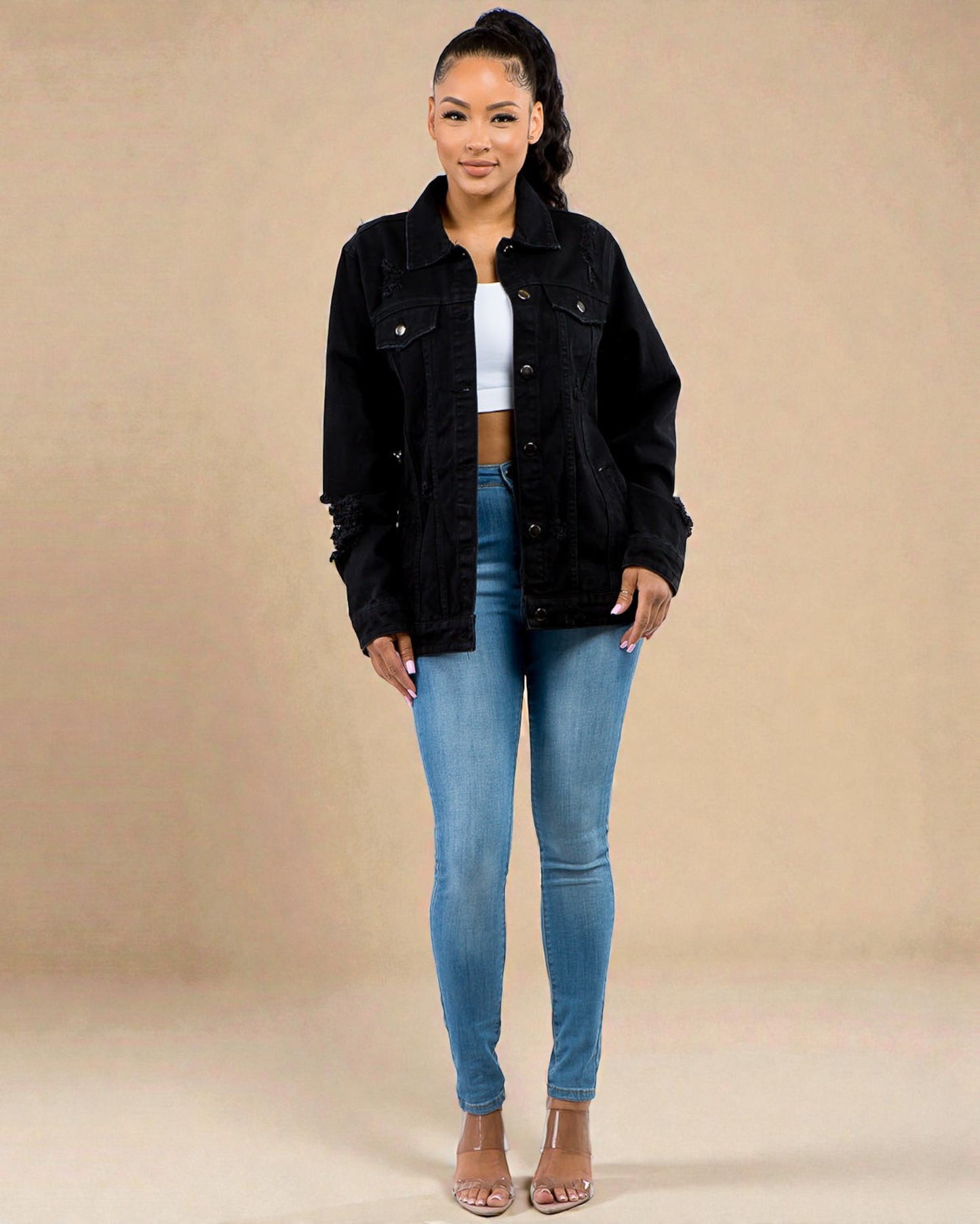 Woman wearing a black jacket and blue jeans against a beige background