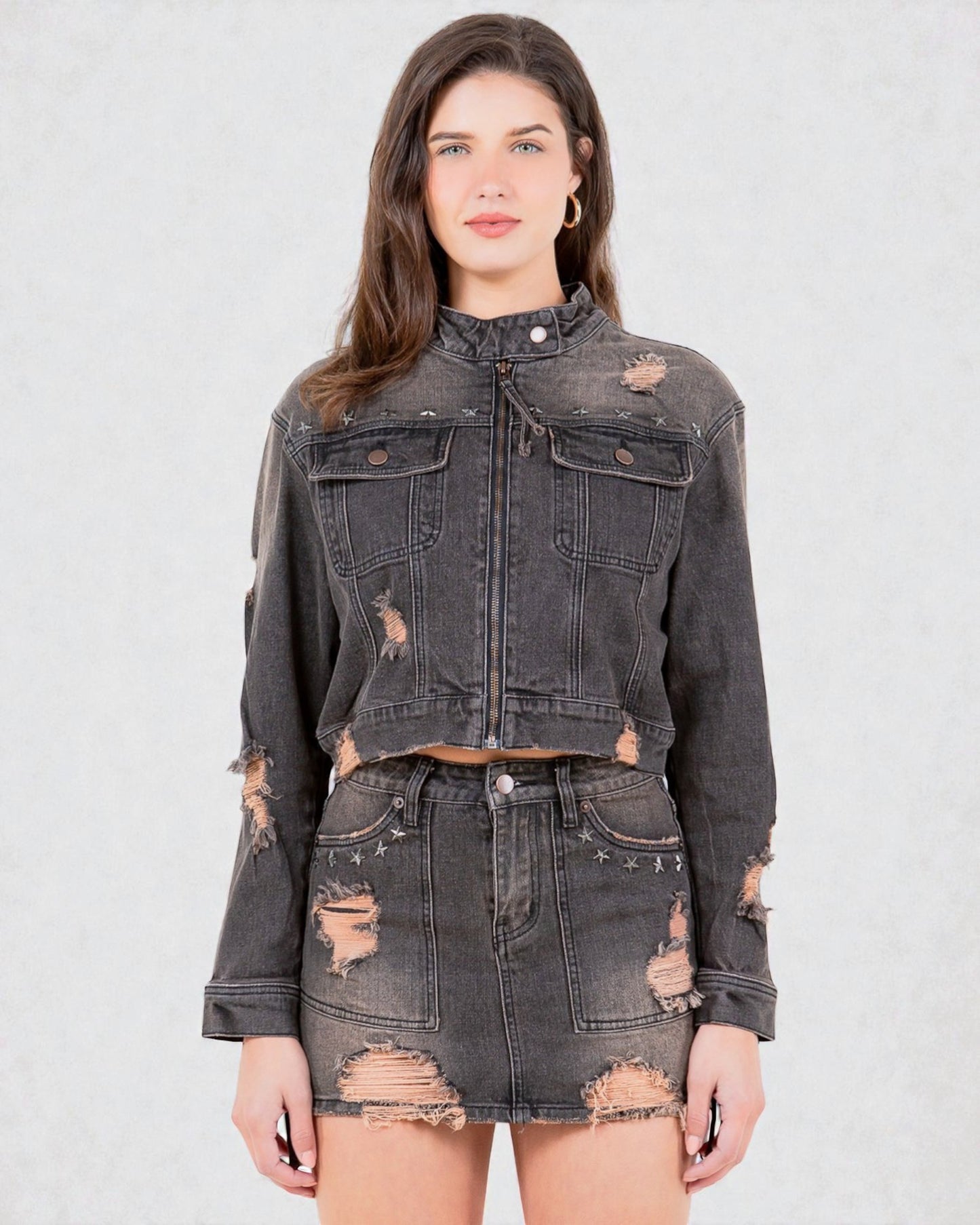 Woman wearing a distressed black denim jacket and skirt on a light gray background