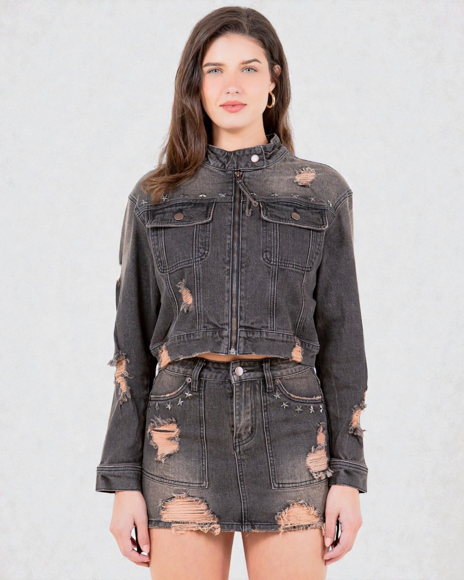 Woman wearing a distressed black denim jacket and skirt on a light gray background