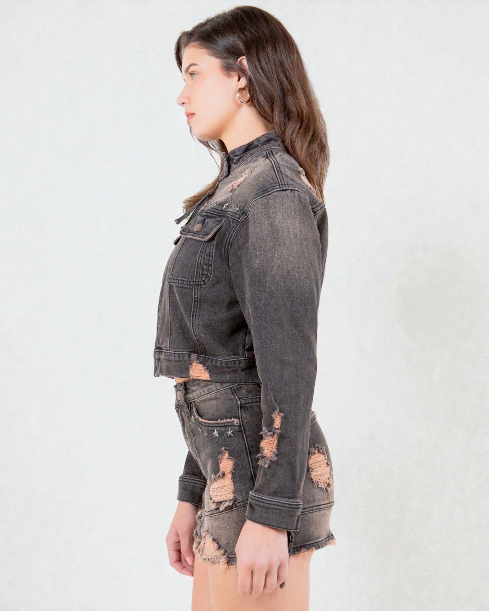 Person wearing a distressed black denim jacket and shorts on a white background