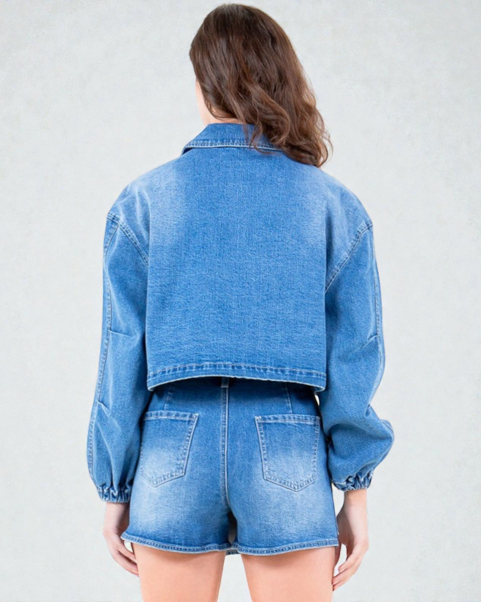 Person wearing a blue denim jacket and shorts on a plain background