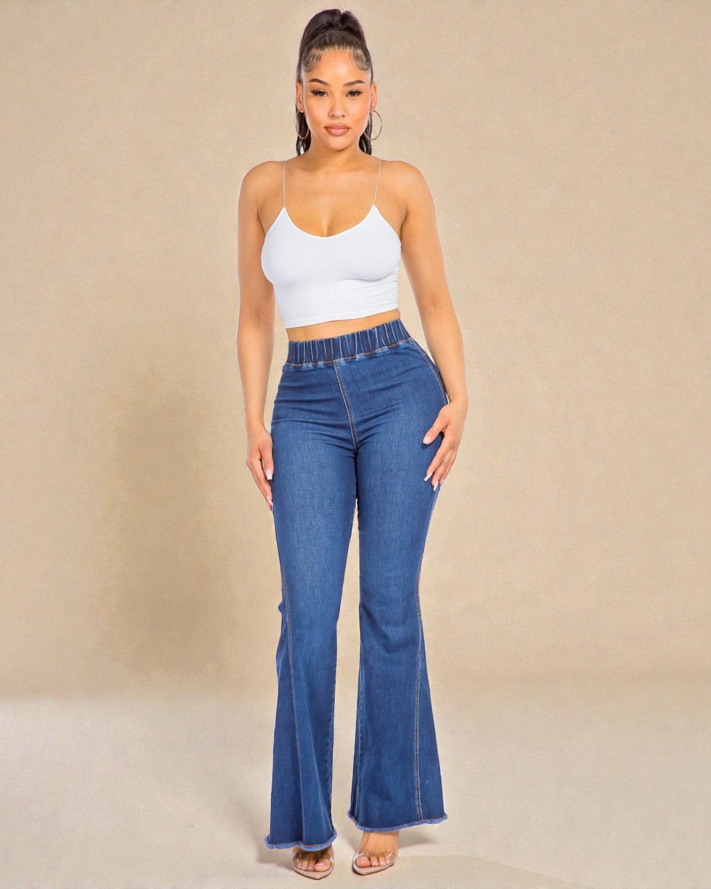 Woman wearing blue flared jeans and a white top against a beige background