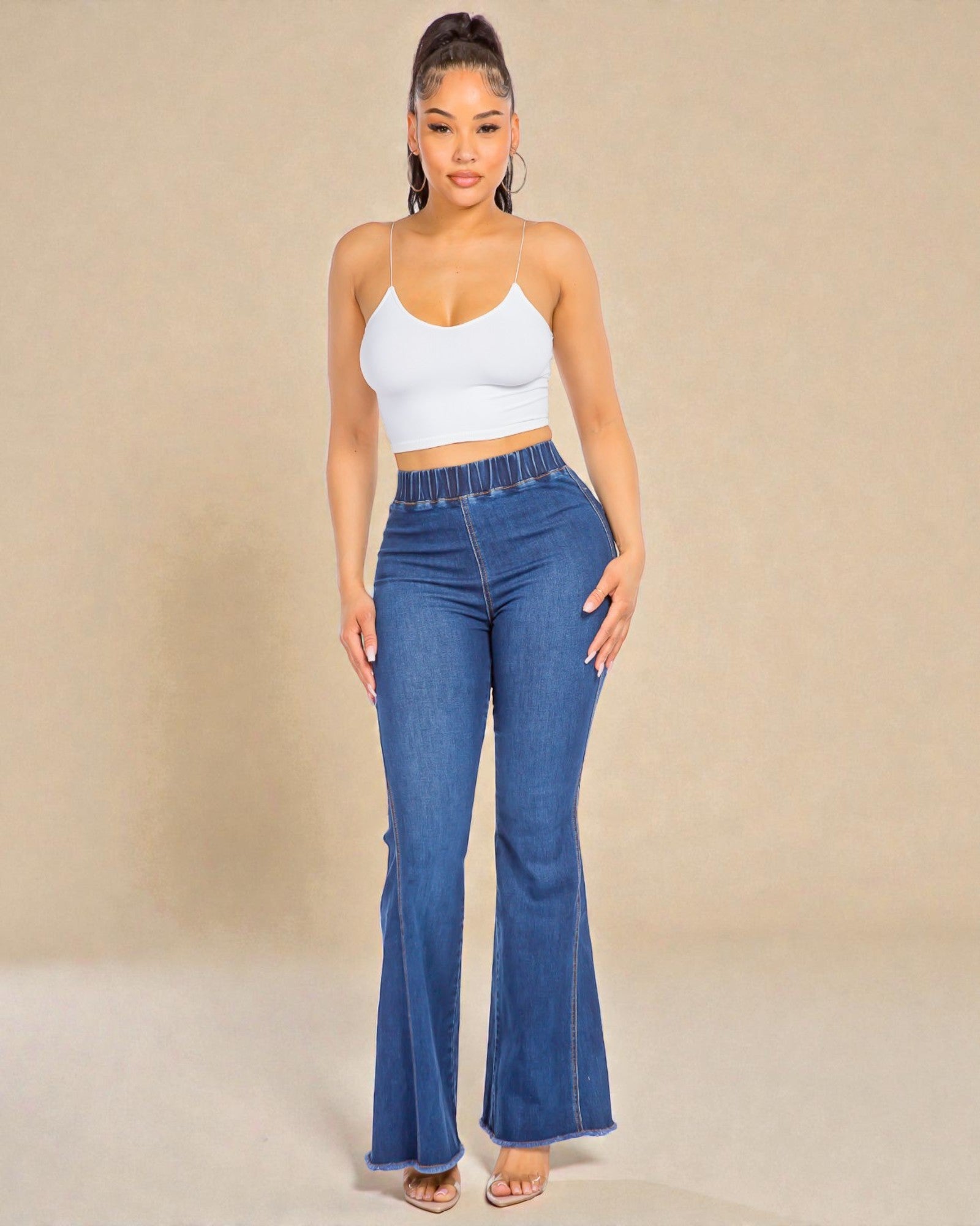 Woman wearing blue flared jeans and a white top against a beige background