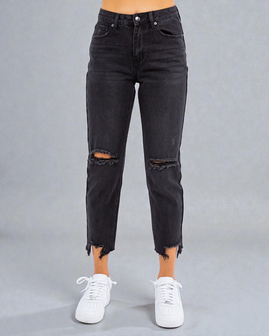 Black distressed jeans worn by a person on a gray background