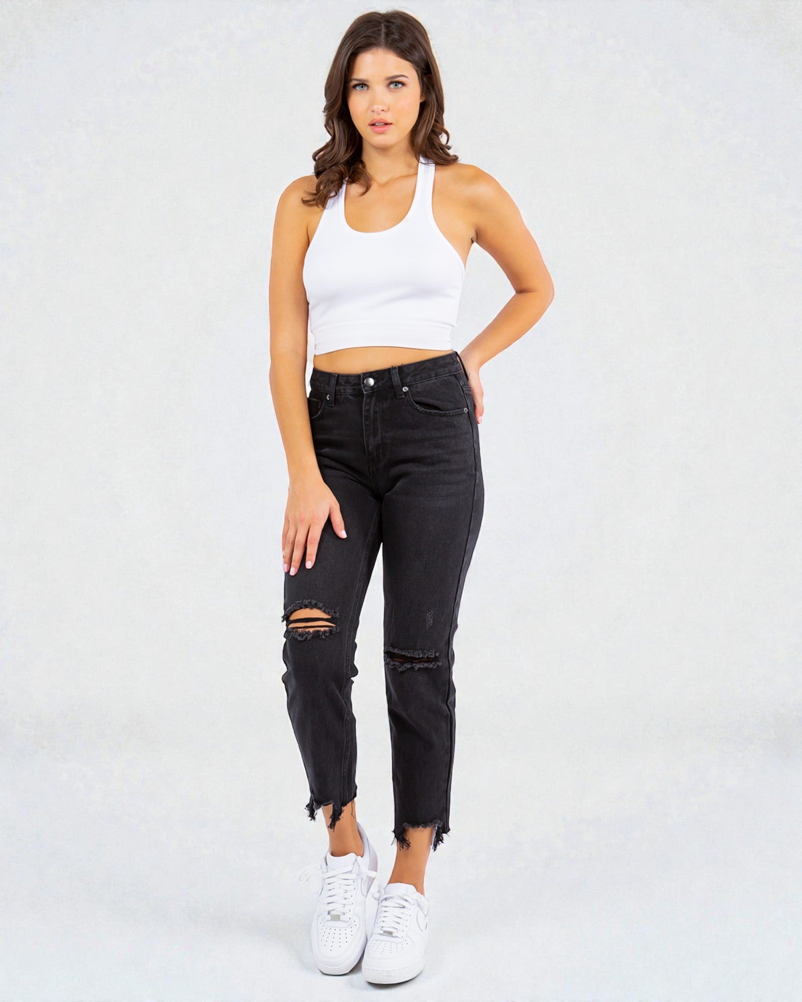 Woman wearing a white tank top and black ripped jeans on a white background