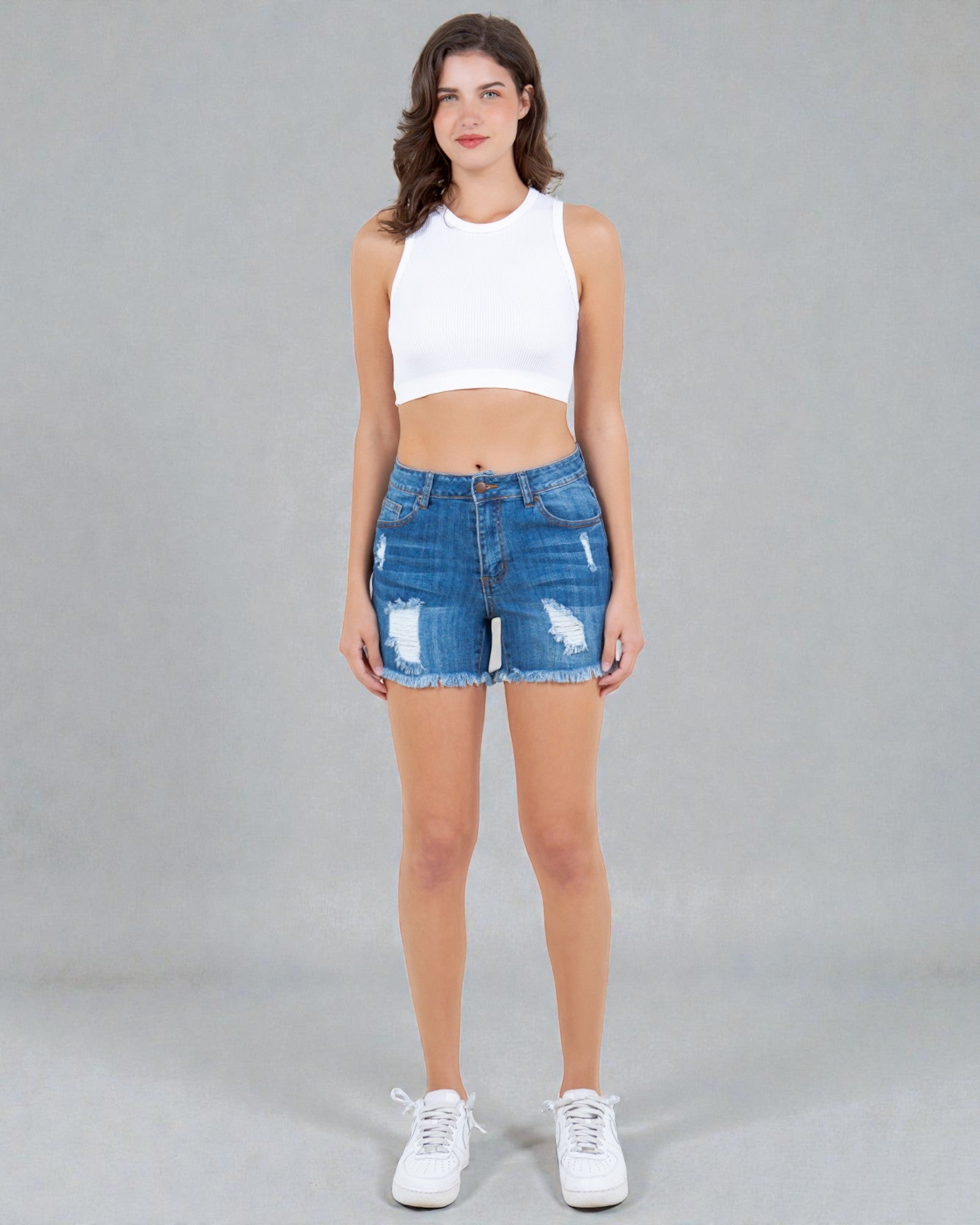 Woman wearing a white crop top and blue denim shorts on a gray background