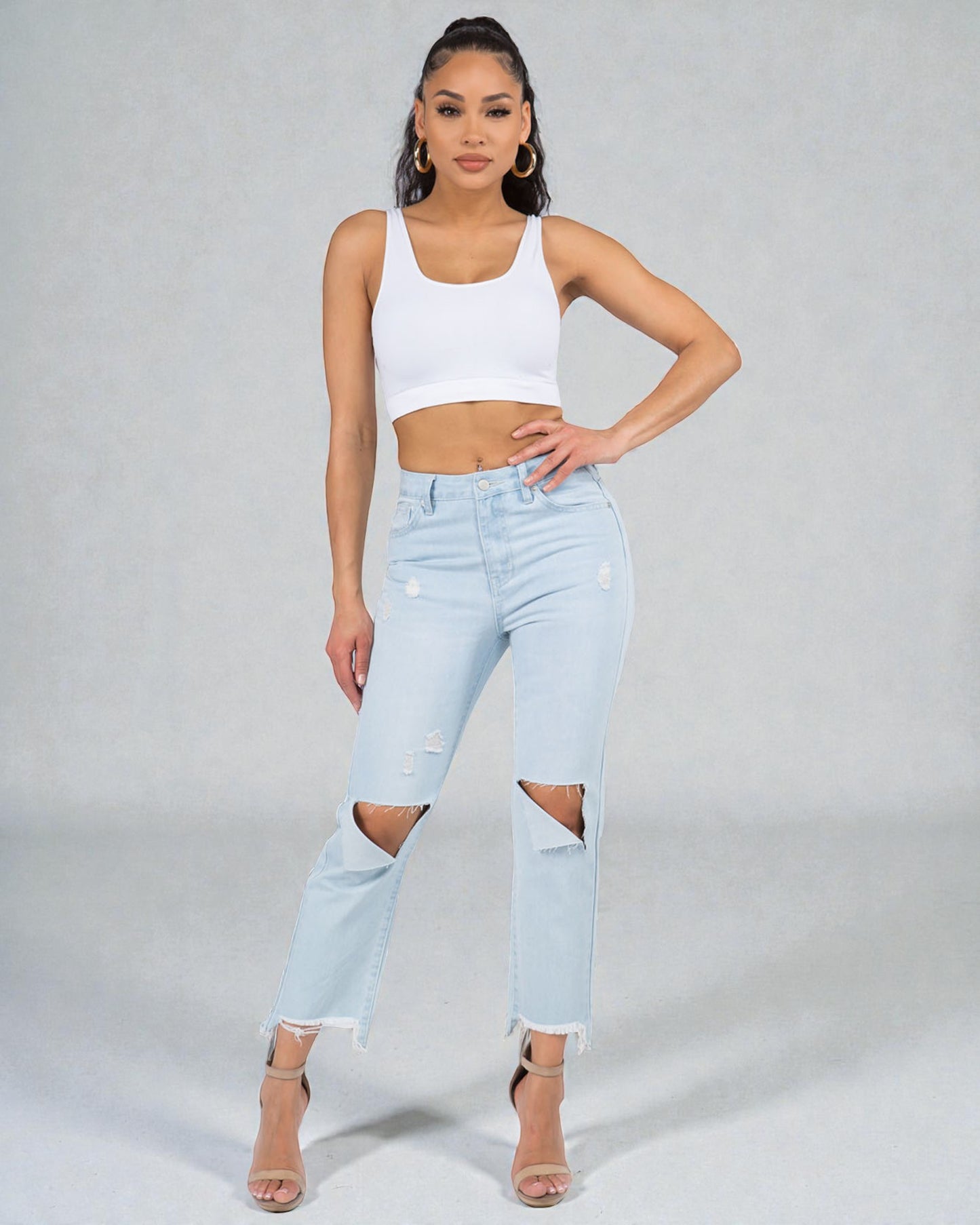 Woman wearing a white crop top and light blue jeans with a gray background