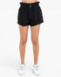 Black high-waisted shorts with a paperbag waistband and button closure, shown on a model from the waist down wearing white sneakers against a plain white background.