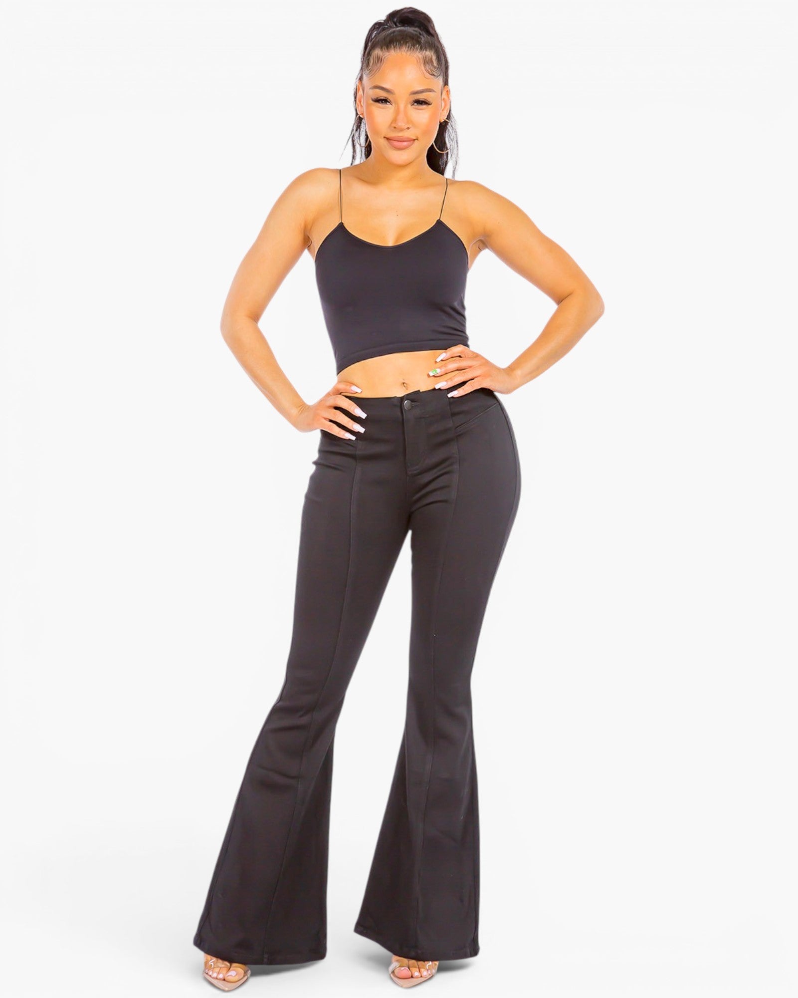 A woman modeling a black two-piece outfit consisting of a spaghetti-strap crop top and high-waisted black flare pants, set against a plain white studio background.