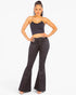 A woman modeling a black two-piece outfit consisting of a spaghetti-strap crop top and high-waisted black flare pants, set against a plain white studio background.