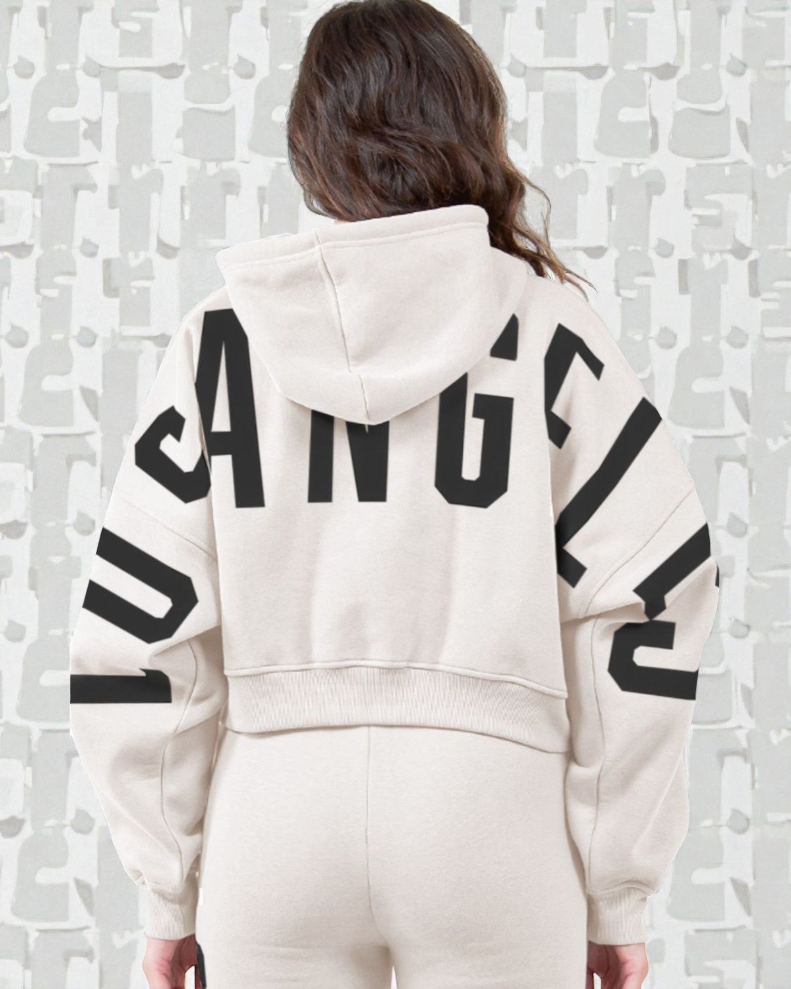 Person wearing a white hoodie with 'Los Angeles' printed on the back against a textured white wall.