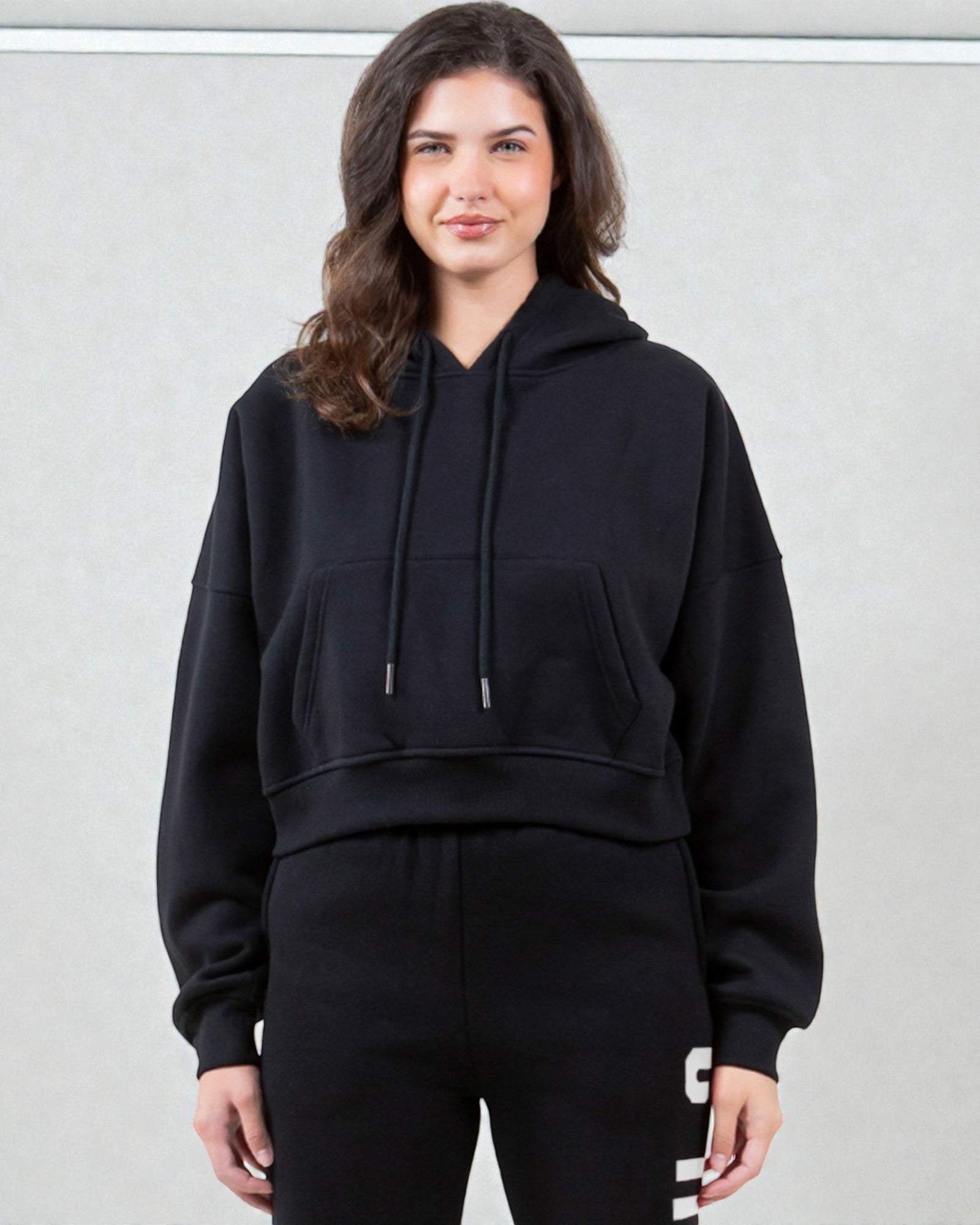 Woman wearing a black hoodie and black pants with white text on a light gray background