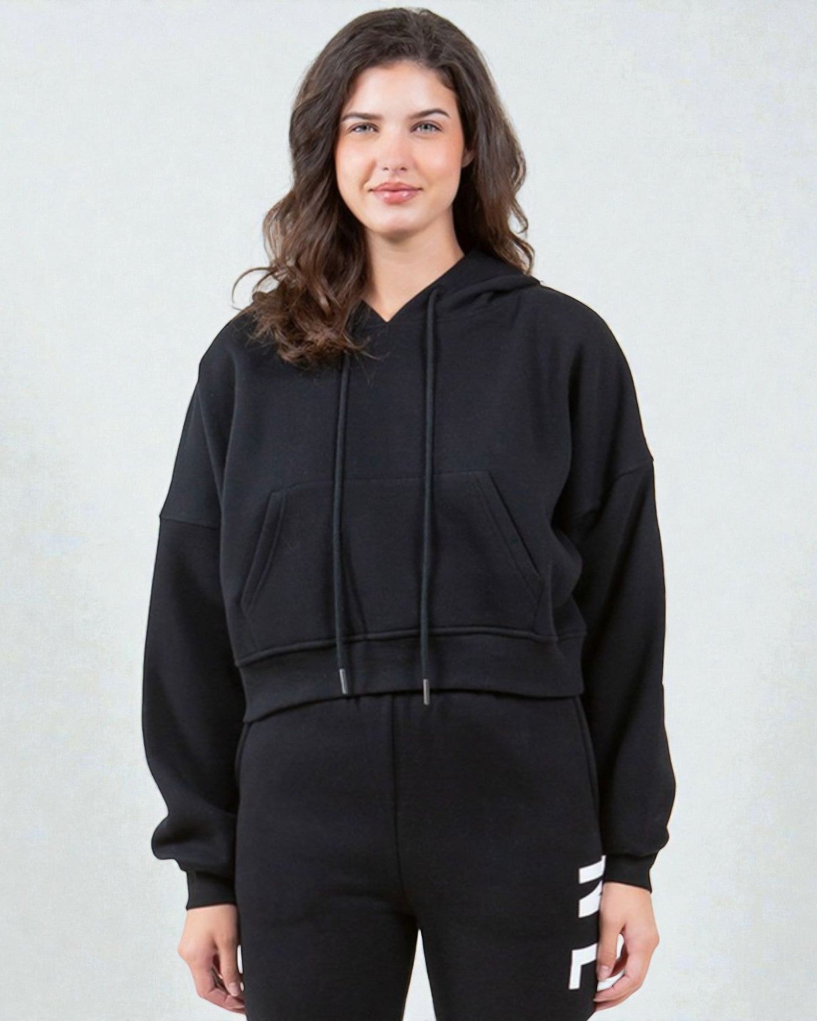 Woman wearing a black hoodie and black pants with white stripes on a light gray background