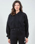 Woman wearing a black hoodie and black pants with white stripes on a light gray background