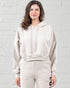 Woman wearing a beige hoodie and pants against a white brick wall