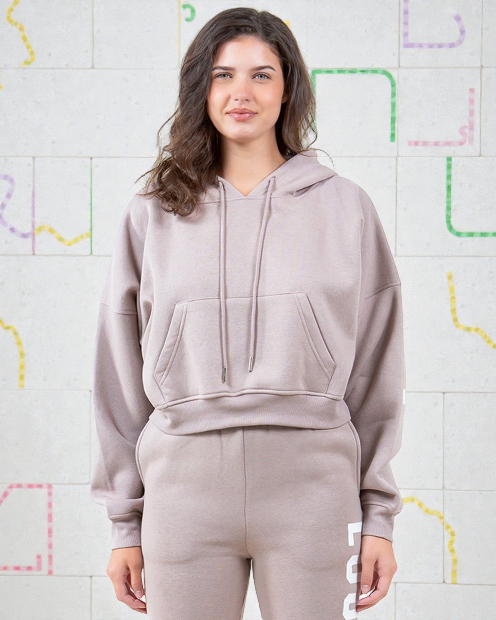 Person wearing a light gray hoodie and pants against a colorful geometric background