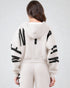 Person wearing a white hoodie with black patterns on sleeves and back against a light gray background