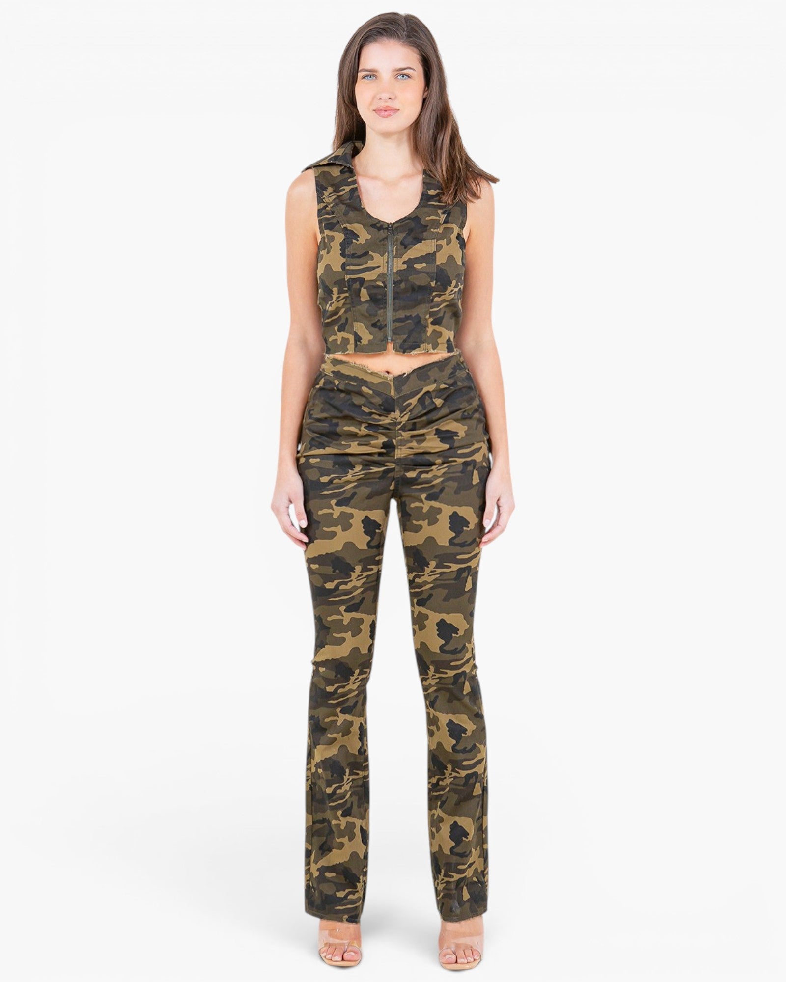 A woman modeling a matching two-piece camouflage set consisting of a sleeveless crop top with a front zipper and high-waisted flared pants, photographed against a plain light gray studio background.