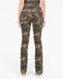 Back view of a model wearing high-waisted camouflage pants with a subtle sheen, paired with beige high-heeled shoes against a plain white background.