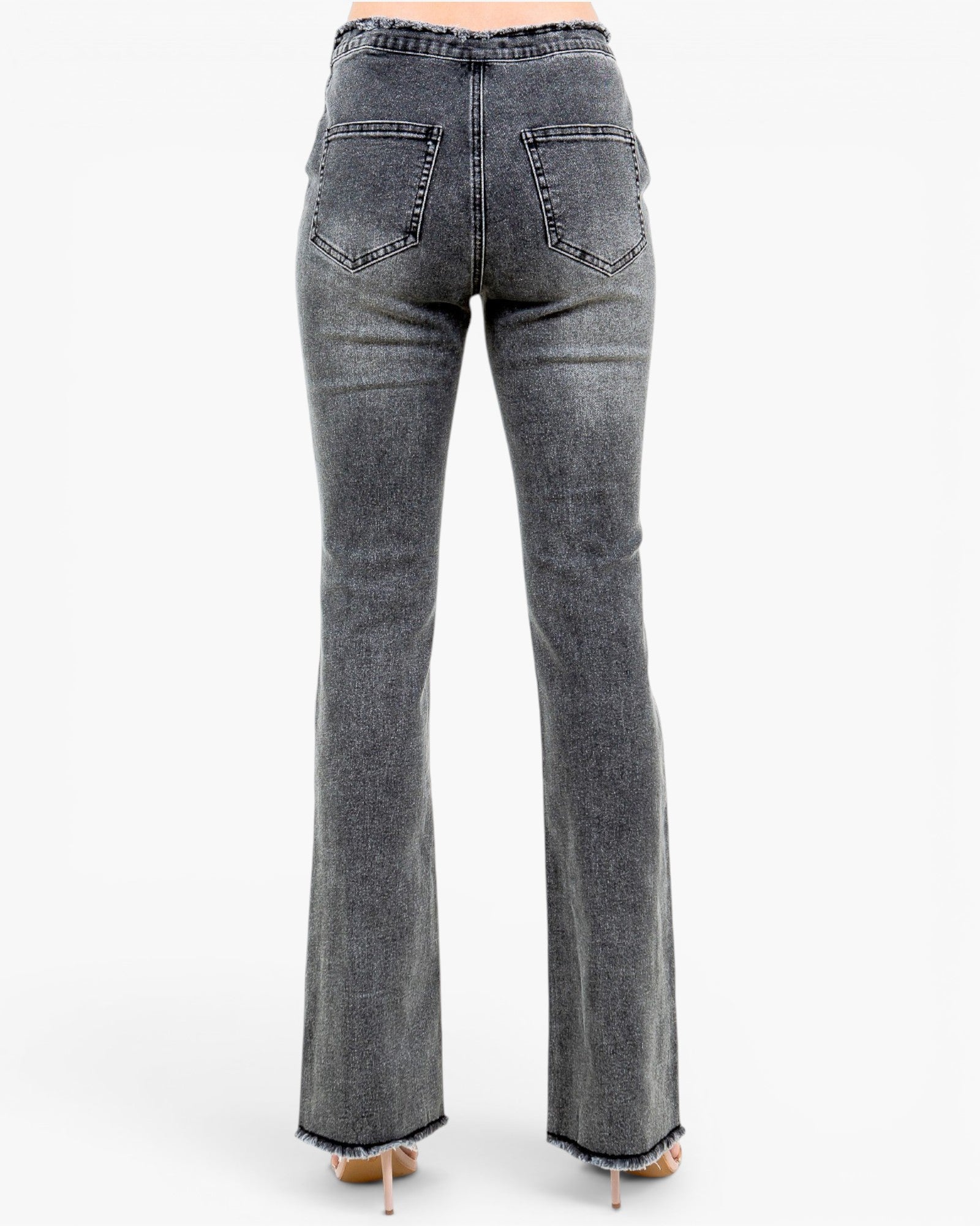 Back view of a person wearing gray denim flare jeans with frayed hems and light-colored high heels, photographed against a plain white studio background.