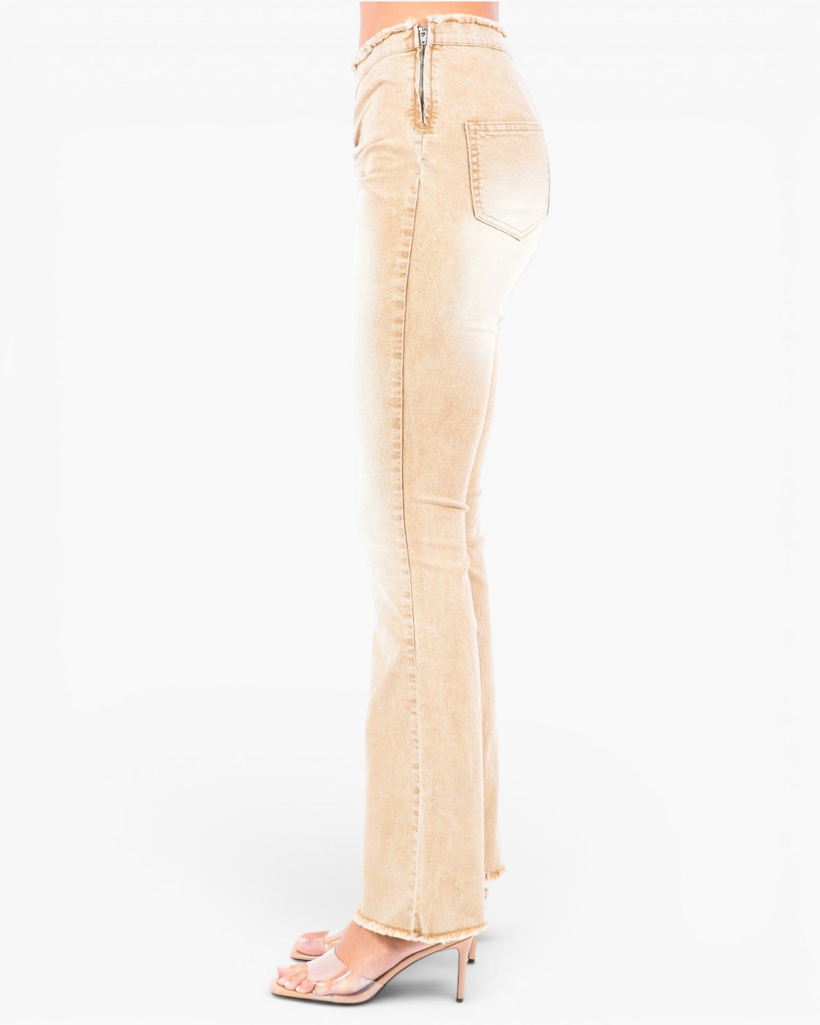 A side profile view of a model wearing light beige flared denim jeans and nude high-heeled sandals against a plain white background.